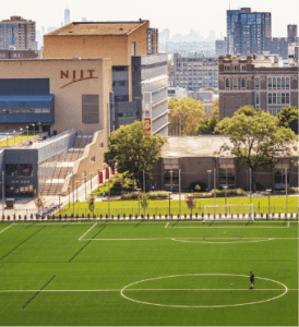 An aerial picture of the New Jersey Institute of Technology (NJIT). A soccer field with one player on it is in the foreground with the buildings of the NJIT campus behind it.