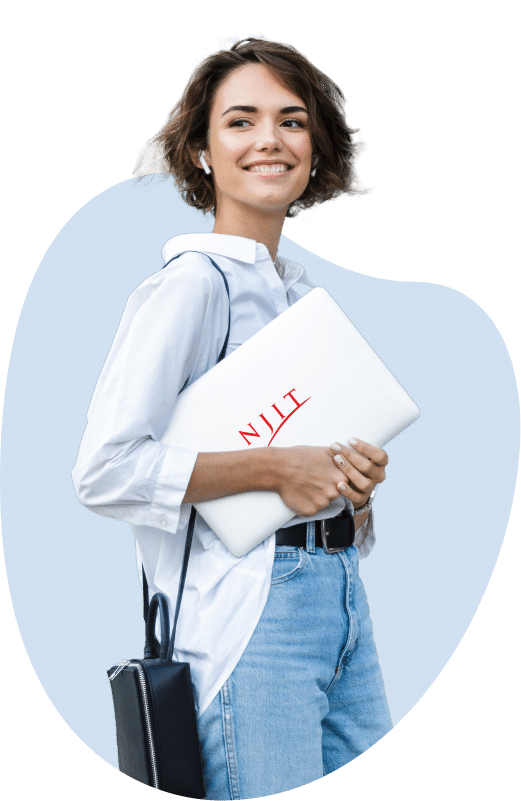 A woman with short dark hair stands while holding a silver laptop with the NJIT logo on it. She has white wireless earbuds in and is wearing light wash jeans, a thick black belt, and a half-tucked white collared shirt.